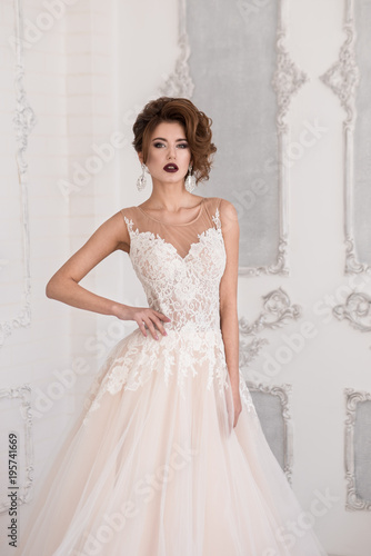 Morning of the bride. A beautiful bride stands in a wedding dress. Wedding hairstyle and makeup. Hand at waist.  Dress with lace.