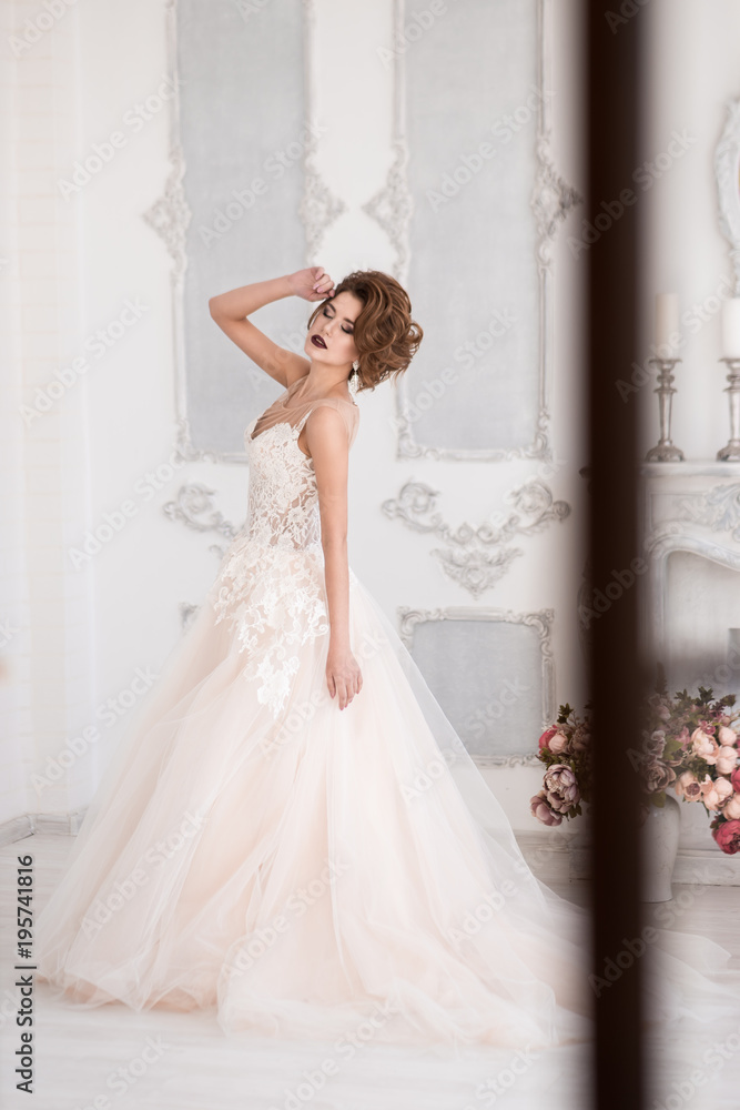 Morning of the bride. A beautiful bride is standing in a lace wedding dress. Wedding hairstyle and makeup. Hand at the face. Spinning in a dress. Photo through the window. Morning of the bride. A beautiful bride is standing in a lace wedding dress. Wedding hairstyle and makeup. Hand at the face. Spinning in a dress. Photo through the window.