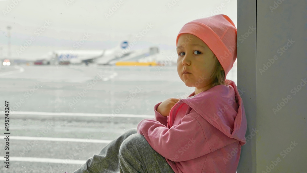 Little girl sits on the floor next to window at airport and looks at camera. Little girl sits on the floor next to window at airport and looks at camera.