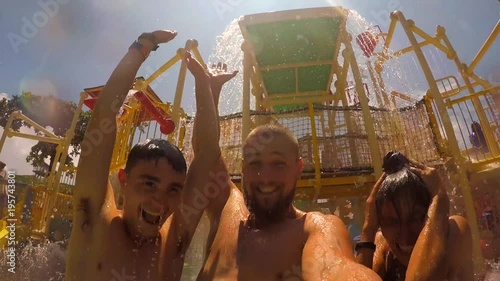 Young Mixed Race Friends Having Fun in Water Park and Making Selfie with GoPro Camera. Waterfall Splash on People Heads in Aquapark. HD Slowmotion.