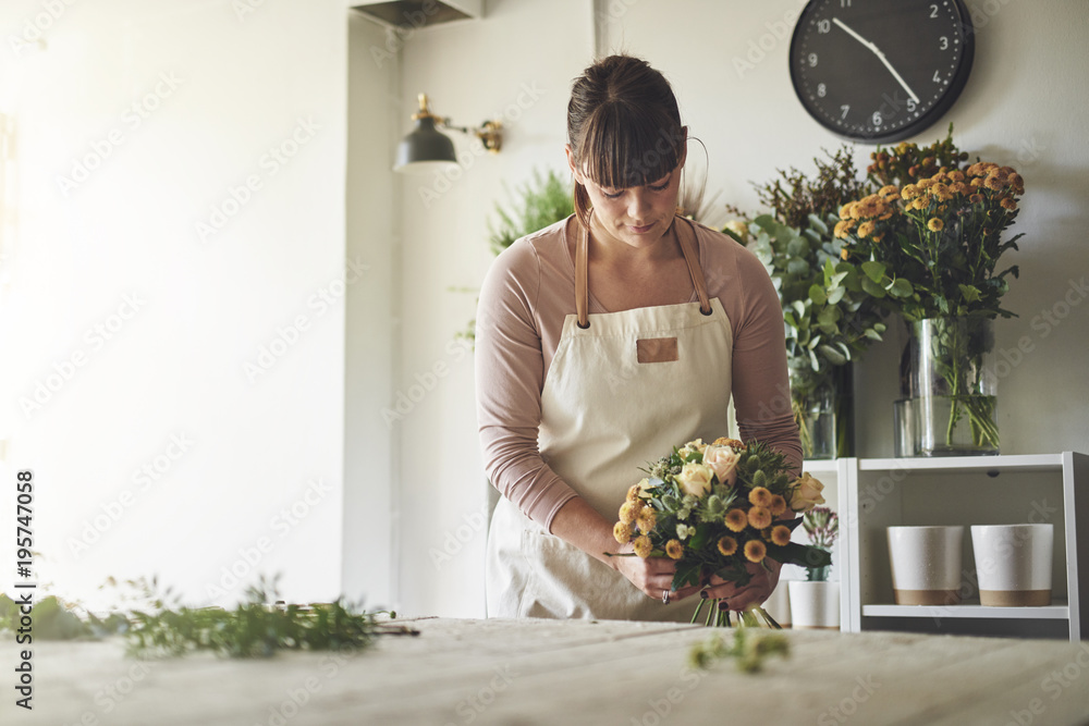 Young florist arranging a mixed flower bouquet in her shop - obrazy, fototapety, plakaty 