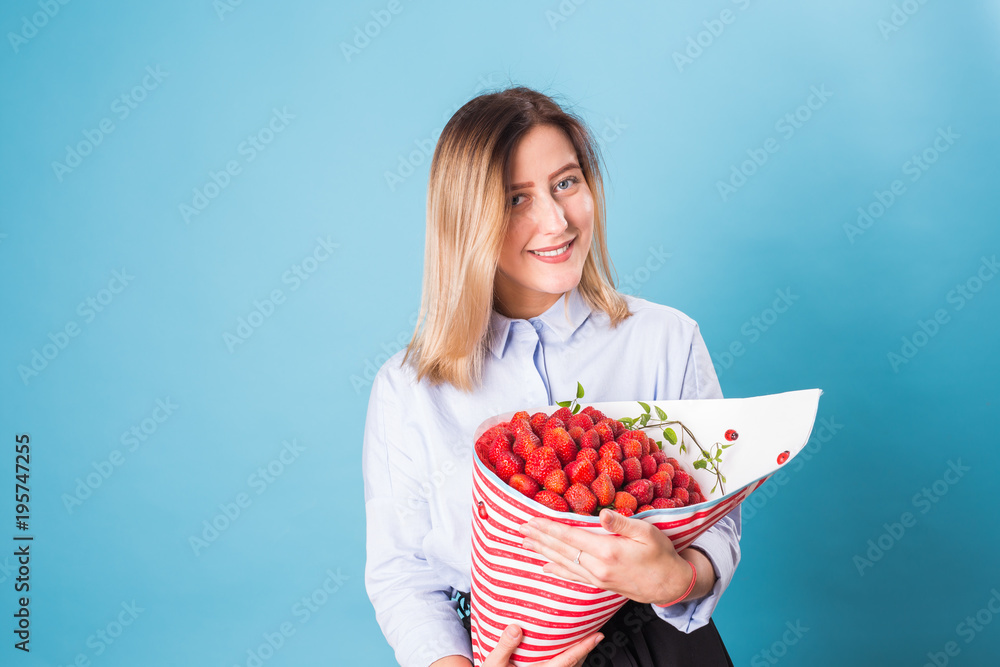 Young woman holding bouquet of strawberries on blue background. Young woman holding bouquet of strawberries on blue background.