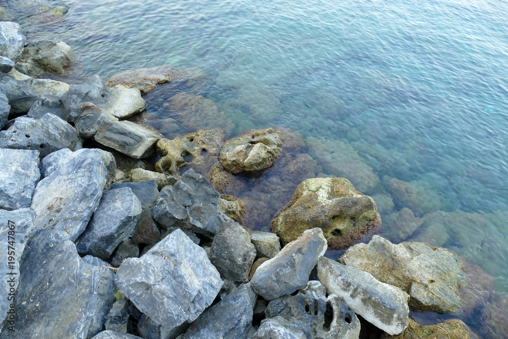 Close up of  a calm sea water and a rocky shore on a summer day