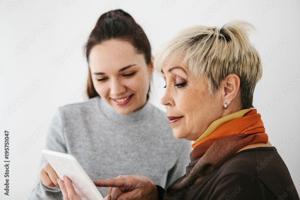 A young girl explains to an elderly woman how to use a tablet or shows some application or teaches you how to use a social network. Teaching the older generation of new technologies. A young girl explains to an elderly woman how to use a tablet or shows some application or teaches you how to use a social network. Teaching the older generation of new technologies.