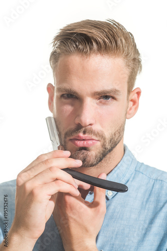 Barbershop concept. Attractive yound barber with beard and mustache while holding straight razor near his beard. Bearded handsome, sexy macho with straight razor in hand poses in studio. Closeup.