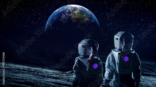 Fototapeta Naklejka Na Ścianę i Meble -  Two Astronauts in Space Suits Standing on the Moon and Look at Beautiful Earth in the Sky. Space Travel, Habitable World and Colonization Concept.