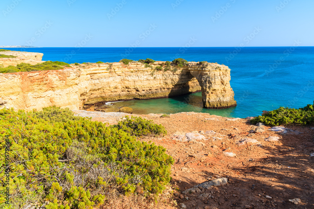 Green plants on cliff and view of rock arch on sea near Armacao de Pera town, Algarve, Portugal