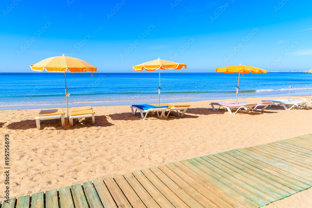 Wooden walkway and sun loungers with umbrellas on beautiful sandy Praia da Rocha beach in Portimao town, Algarve, Portugal