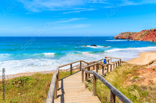 Young woman tourist walking to Amado beach on wooden walkway, Algarve, Portugal