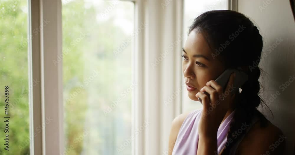 4K Serious woman standing next to window talking on cell phone as rain falls outside. Slow motion. 4K Serious woman standing next to window talking on cell phone as rain falls outside. Slow motion.