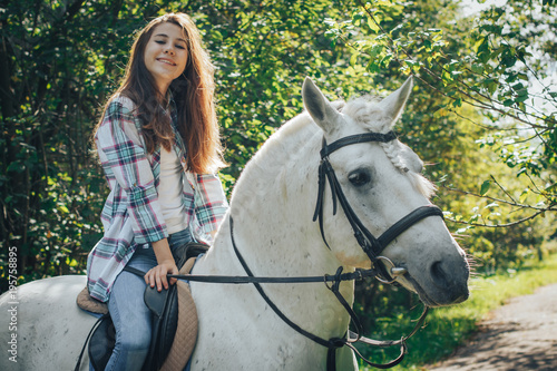 Girl teenager and white horse in a park in a summer