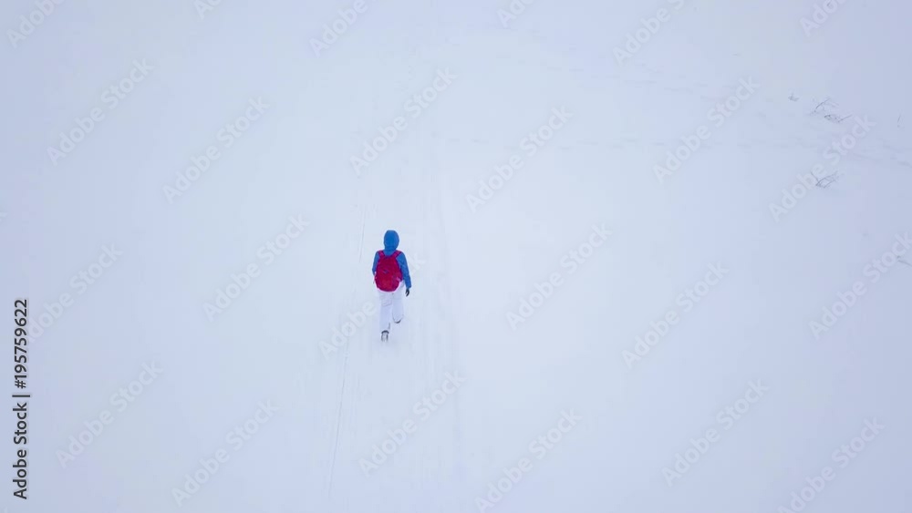 Flight over the lonely tourist girl walking along the top of a mountain covered with snow. Snowy frosty weather Flight over the lonely tourist girl walking along the top of a mountain covered with snow. Snowy frosty weather