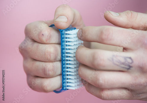 a young man holds a nail brush on a pink background photo