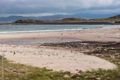 Mellon Udrigle  Scotland - June 8  2012  Sandy Atlantic Ocean beach under heavy rainy blue-gray sky . Pebbles in sand. Dark foggy hills in back.