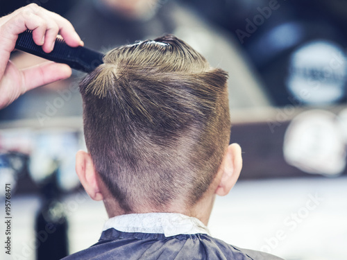 Boy getting haircut by hairdresser in London barbershop.