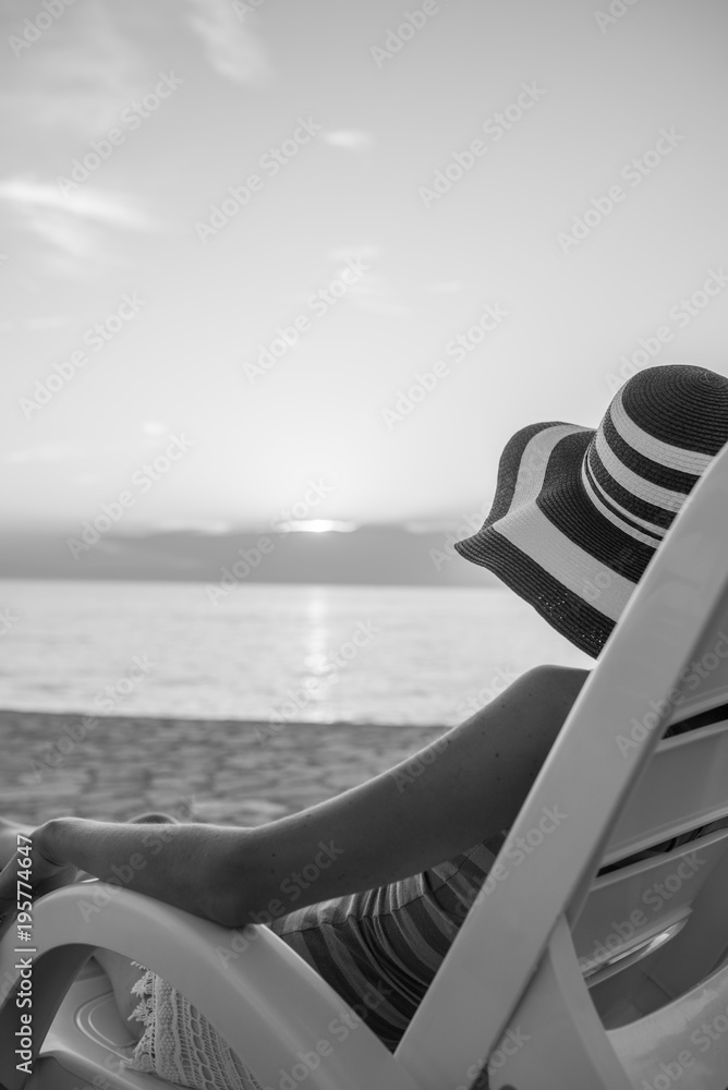 Lonely woman looking at sunset as she relaxes on a recliner chair on the beach on summer vacation