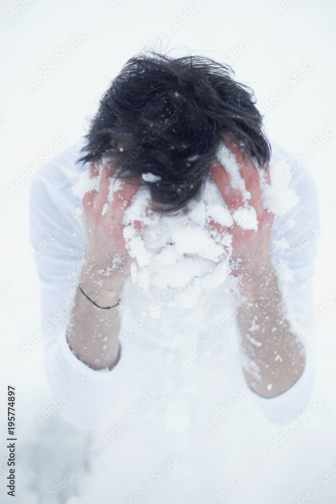 Vertical close up portrait of brunette male dressed in t-shirt starting cold winter morning with washing face with white snow to promote health, sitting on knees at ground. Wellness and beauty concept Vertical close up portrait of brunette male dressed in t-shirt starting cold winter morning with washing face with white snow to promote health, sitting on knees at ground. Wellness and beauty concept