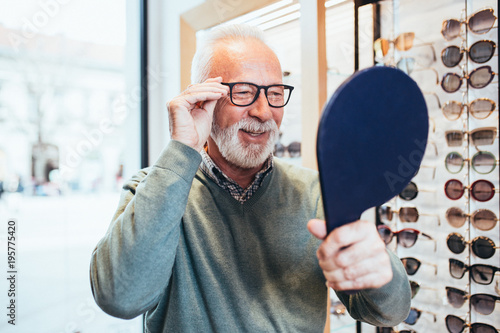 Handsome senior man choosing eyeglasses frame in optical store.  photo
