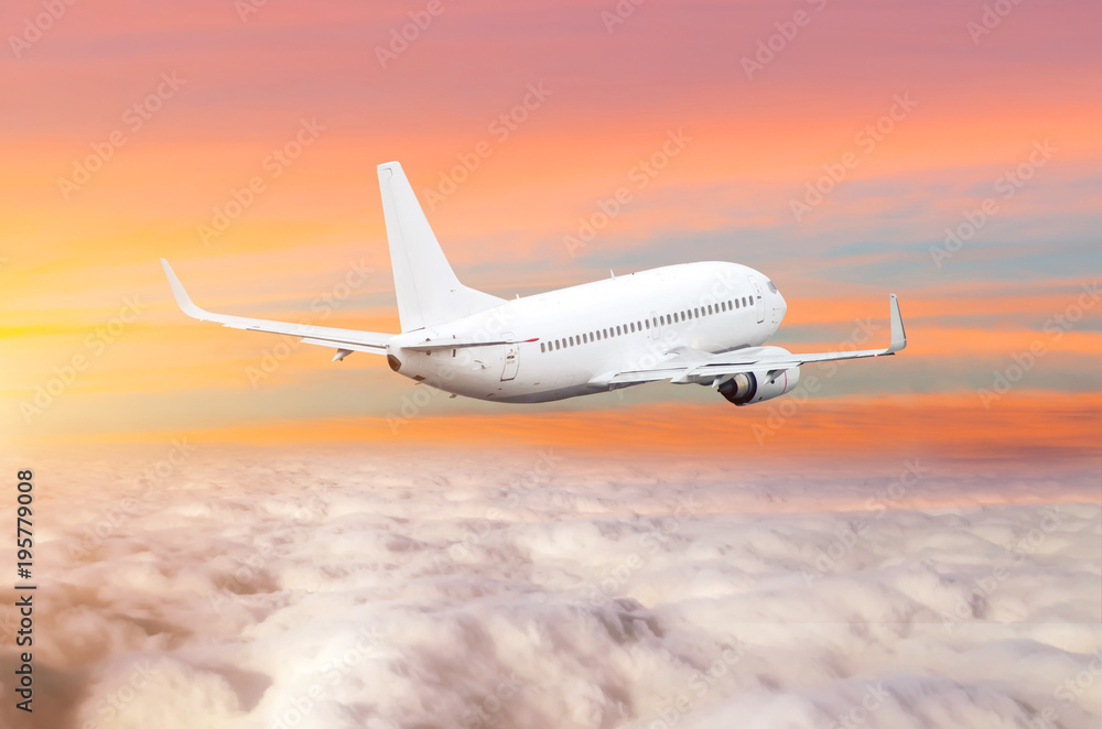 Obraz premium Passanger airplane above the clouds horizon sky with bright sunset colors.