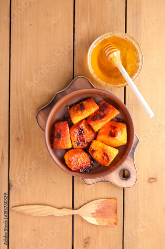 Pumpkin, baked pumpkin with honey, pottery on a wooden background, rustic style, slices of pumpkin on a wooden board, vegetarianism, healthy food, baked in the oven vegetables with honey, minimalism