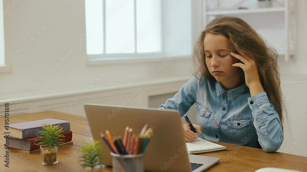 Young girl with laptop computer is doing homework. College education. Tired Female student studying and using pc at home. Young girl with laptop computer is doing homework. College education. Tired Female student studying and using pc at home.