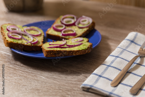 three avocado toast with salt and pepper and red onion cut in rings on a blue plate