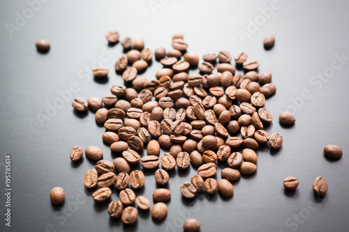 The grains of roasted coffee are scattered on a black matte surface