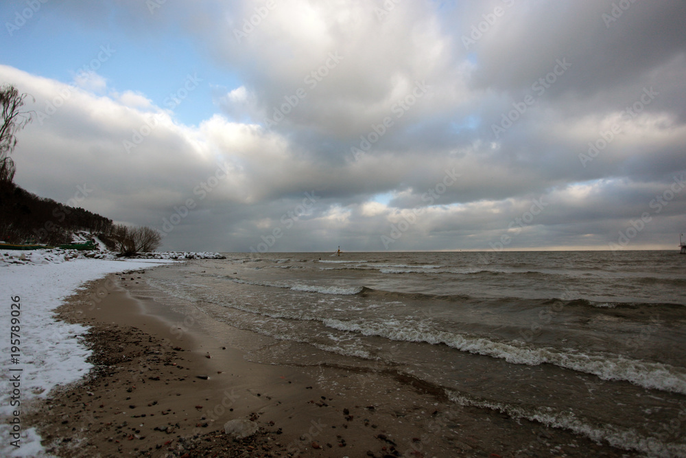 Baltic sea winter landscape -   snowy beach with  and  the sea with rocks in the background with bright blue  sky with clouds on a sunny winter day