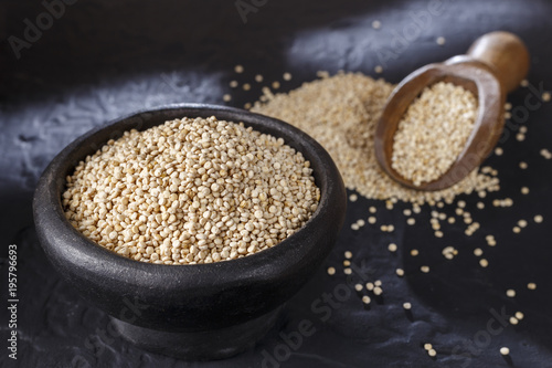 Quinoa grains with spoon and bowl on black background