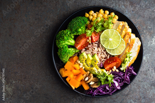Buddha bowl meal with chicken fillet, brown rice, avocado, pepper, tomato, broccoli, red cabbage, chickpea, fresh lettuce salad, pine nuts and walnuts. Healthy balanced eating. Overhead view