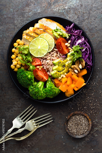 Buddha bowl meal with chicken fillet, brown rice, avocado, pepper, tomato, broccoli, red cabbage, chickpea, fresh lettuce salad, pine nuts and walnuts. Healthy balanced eating. Overhead view