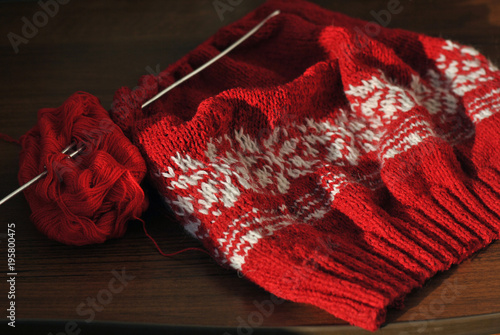 Needlework. Homemade knitting from red and white wool with knitting needles. Close-up.