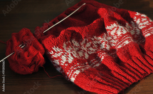 Needlework. Homemade knitting from red and white wool with knitting needles. Close-up.