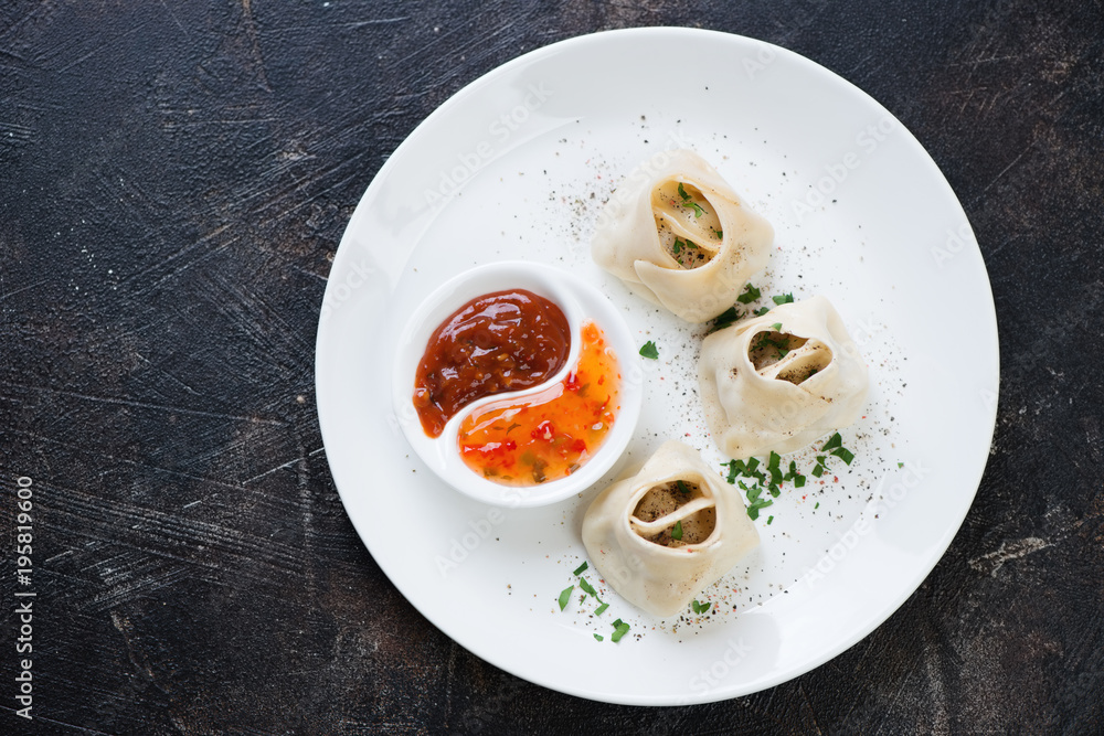 White plate with manti or steamed meat dumplings on a dark brown stone background, view from above, horizontal shot White plate with manti or steamed meat dumplings on a dark brown stone background, view from above, horizontal shot