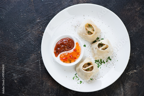 White plate with manti or steamed meat dumplings on a dark brown stone background, view from above, horizontal shot