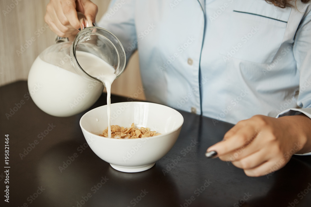 Girlfriend preparing simple breakfast in morning. Cropped shot of woman in nightwear pouring milk in bowl with cereals, wanting to eat fast and getting dressed to go to office Girlfriend preparing simple breakfast in morning. Cropped shot of woman in nightwear pouring milk in bowl with cereals, wanting to eat fast and getting dressed to go to office