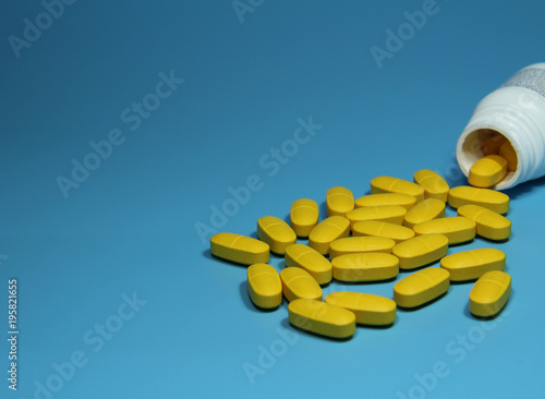 Yellow color Pills scattered on blue background and white pharmacy bottle