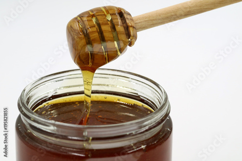 A close up of a honey jar and a honey spoon on a white background
