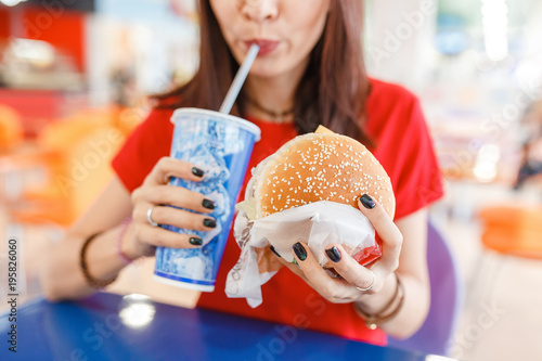 Woman drinking soda with burger in Fast food court in the mall