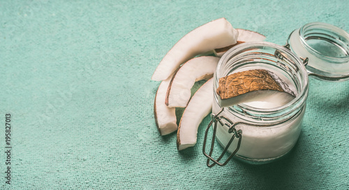 Coconut milk in glass jar with coconut slices on turquoise background with copy space