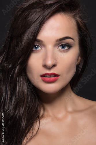 Portrait of a beautiful young girl with dark long hair and professional make-up on a black background.