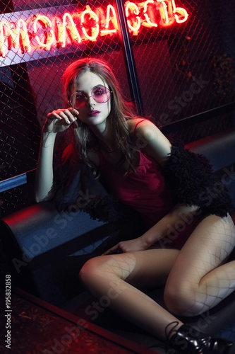 Girl, model in a black, fashionable fur coat and sunglasses in a nightclub. Fashion, style, beauty, night life.