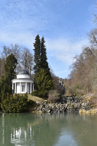 Beautiful nature with a small lake and a waterfall with a white chapel at World Cultural Heritage Herkules in Kassel, Wilhelmshöhe, Germany