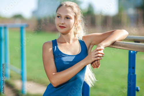 portrait of Pretty fit girl in a blue shirt and leggings with ideal body in sport place. fit and sporty woman training outside