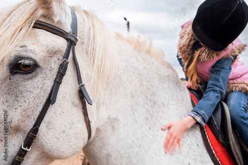 little girl sitting on horseback and stroking her