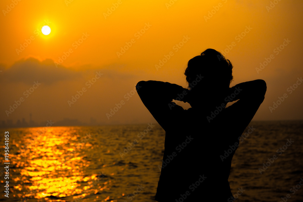 silhouette of behind a man is standing to looking sunset on city beside sea. relaxation and traveling concept.