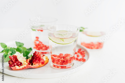 detox water in a glass with pomegranate seeds, mint leaves and lime on a white background, selective focus