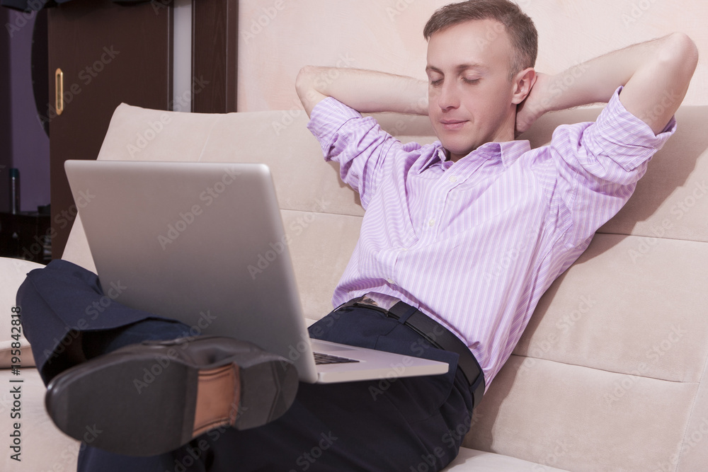 Relaxing Man in Business Style Clothing and Formal Penny Loafers Shoes Sitting on Couch while Legs Folded. Posing with Laptop Computer.