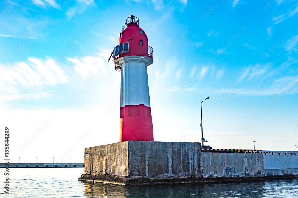 Navigation lighthouse tower on the breakwater in the seaport.