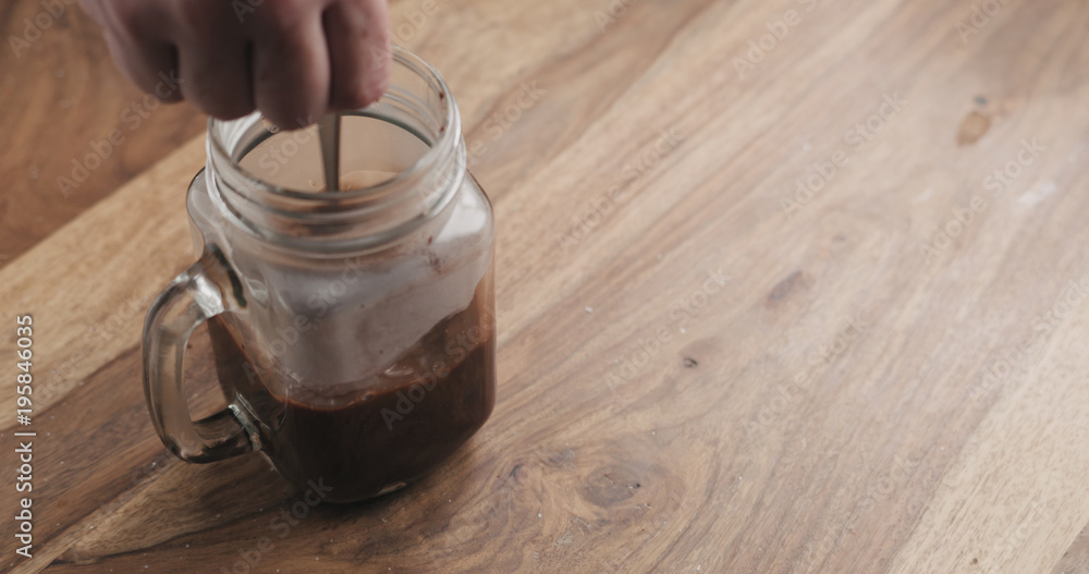 Obraz premium making cocoa drink in glass jar with handle on wood table, stirring cocoa